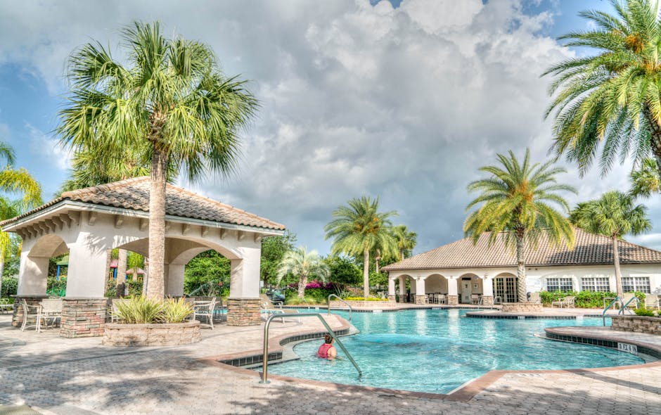 Beautiful tropical resort poolside scene featuring palm trees and inviting water under a cloudy sky.