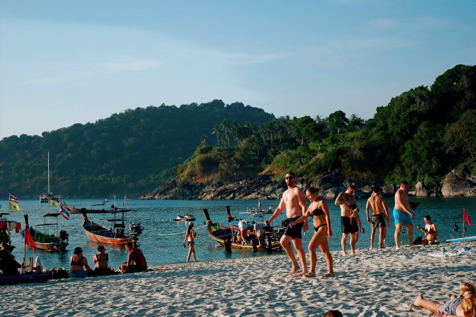 Tourists enjoy a sunny day at a tropical beach with boats and lush greenery